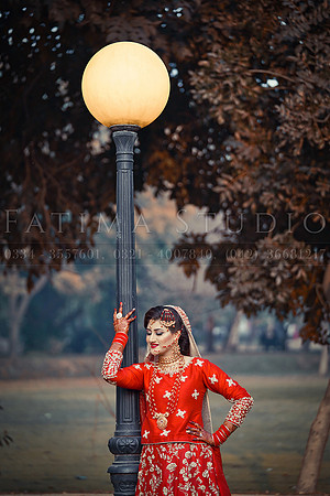 Bride wearing a traditional red dress posing by lamp pole in a park