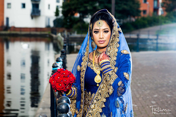bride standing by the lake holding a bouquet of red roses wearing a blue wedding dress